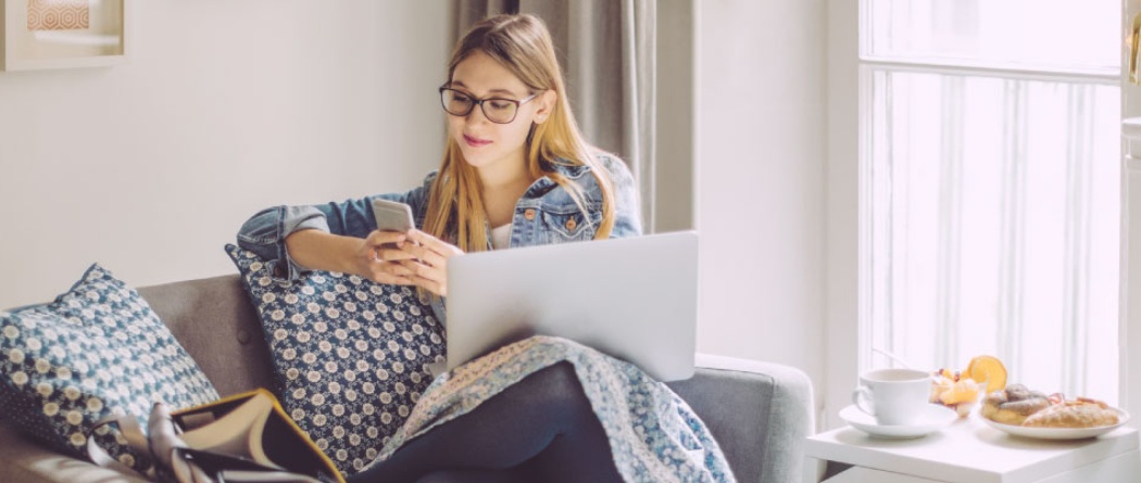 a woman sitting on her couch holding a mobile phone with her laptop computer